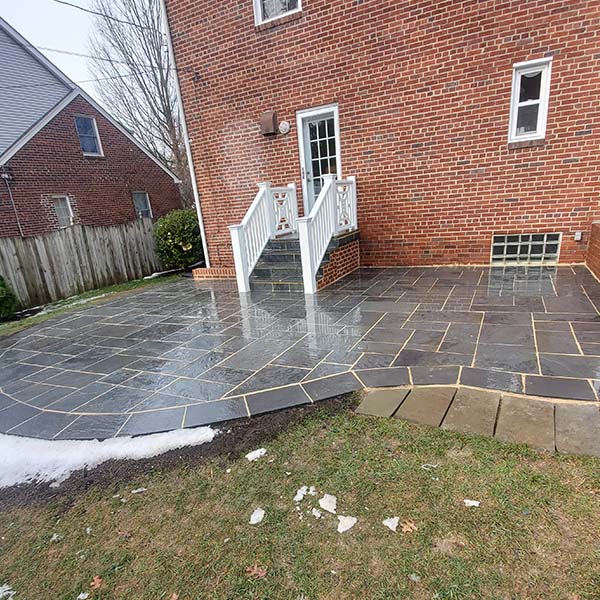 Red brick house with white door and steps opens to a wet, neatly-tiled patio with stone borders