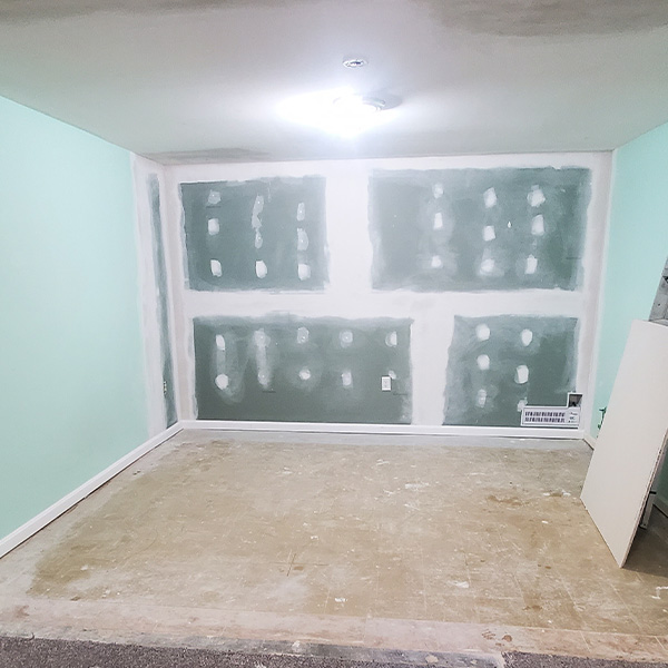 Unfinished room with drywall patches on a green wall, concrete floor, and unfinished ceiling
