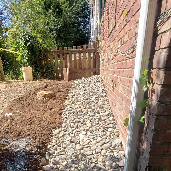 A narrow stone path lined with smooth, gray pebbles runs along a red brick wall.